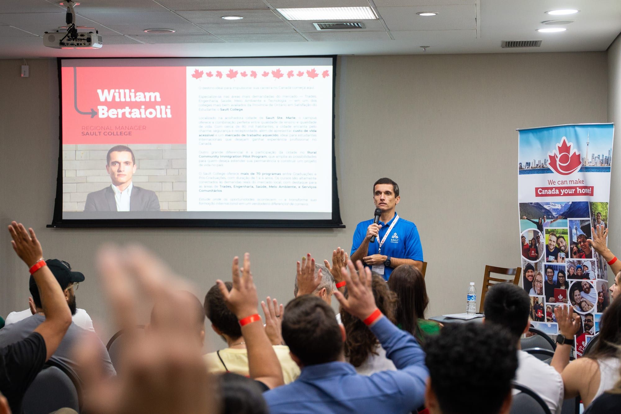 Sala de painéis cheia, com participantes de mãos levantadas